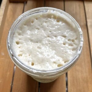 bubbly sourdough starter in a glass pint jar sitting on a wooden tray