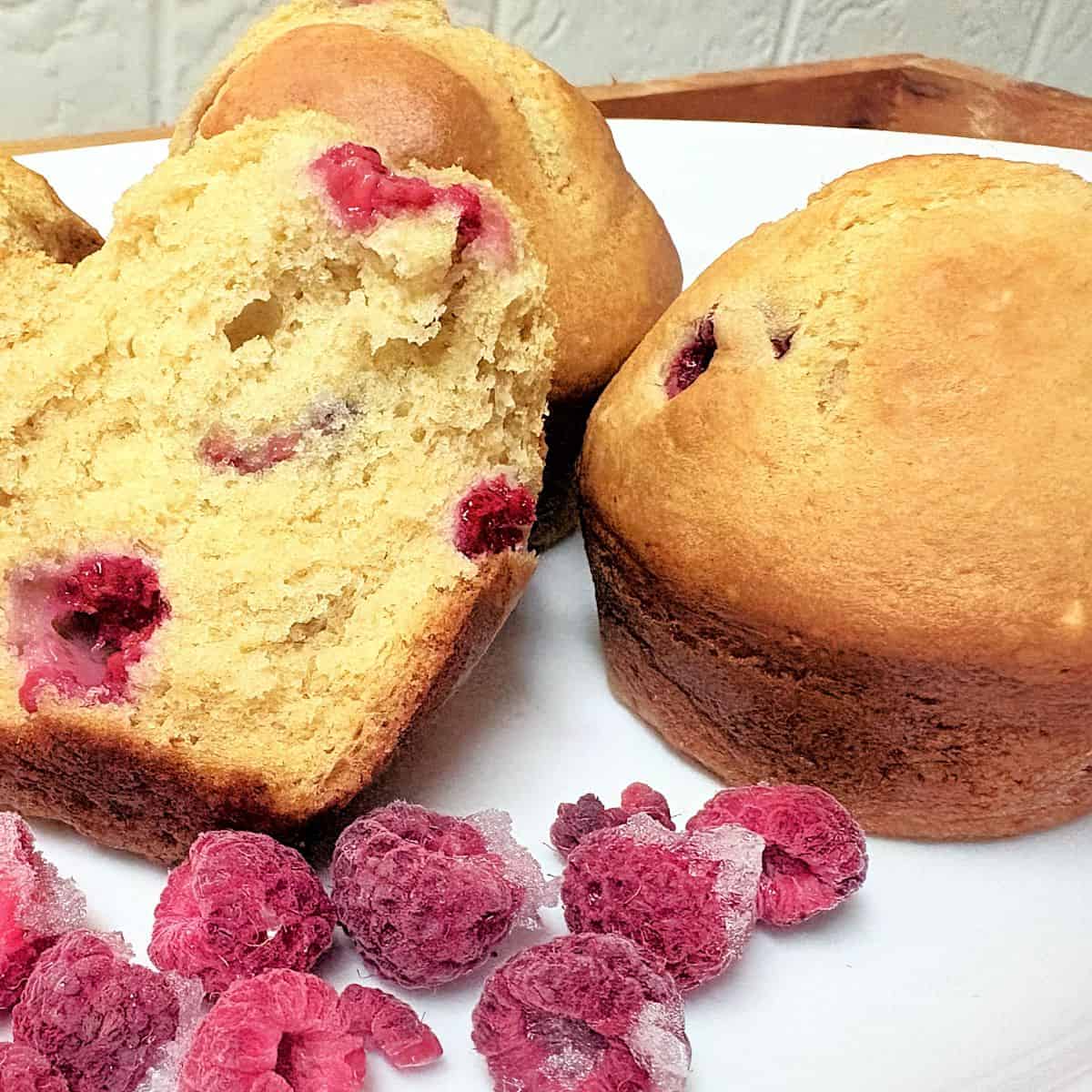 raspberry muffins on a white plate with frozen raspberries
