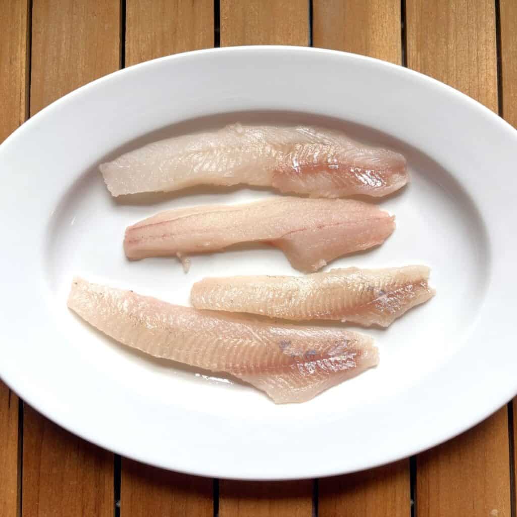 fresh fish fillets laying on a white plate on a wooden tray
