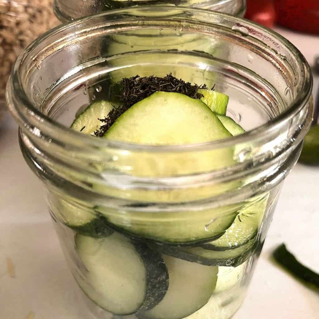 sliced cucumbers in a pint jar with dill