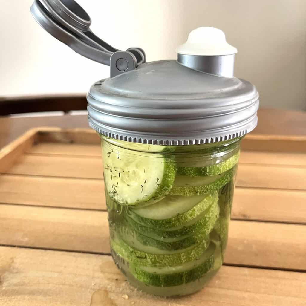 lacto fermented pickles in a pint jar with a fermentation lid