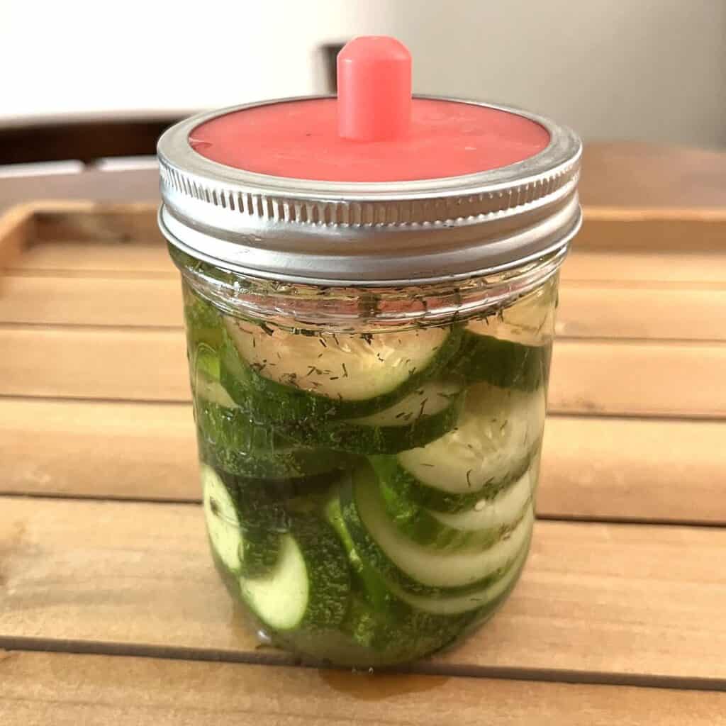 lacto fermented pickles in a pint jar with a fermentation lid