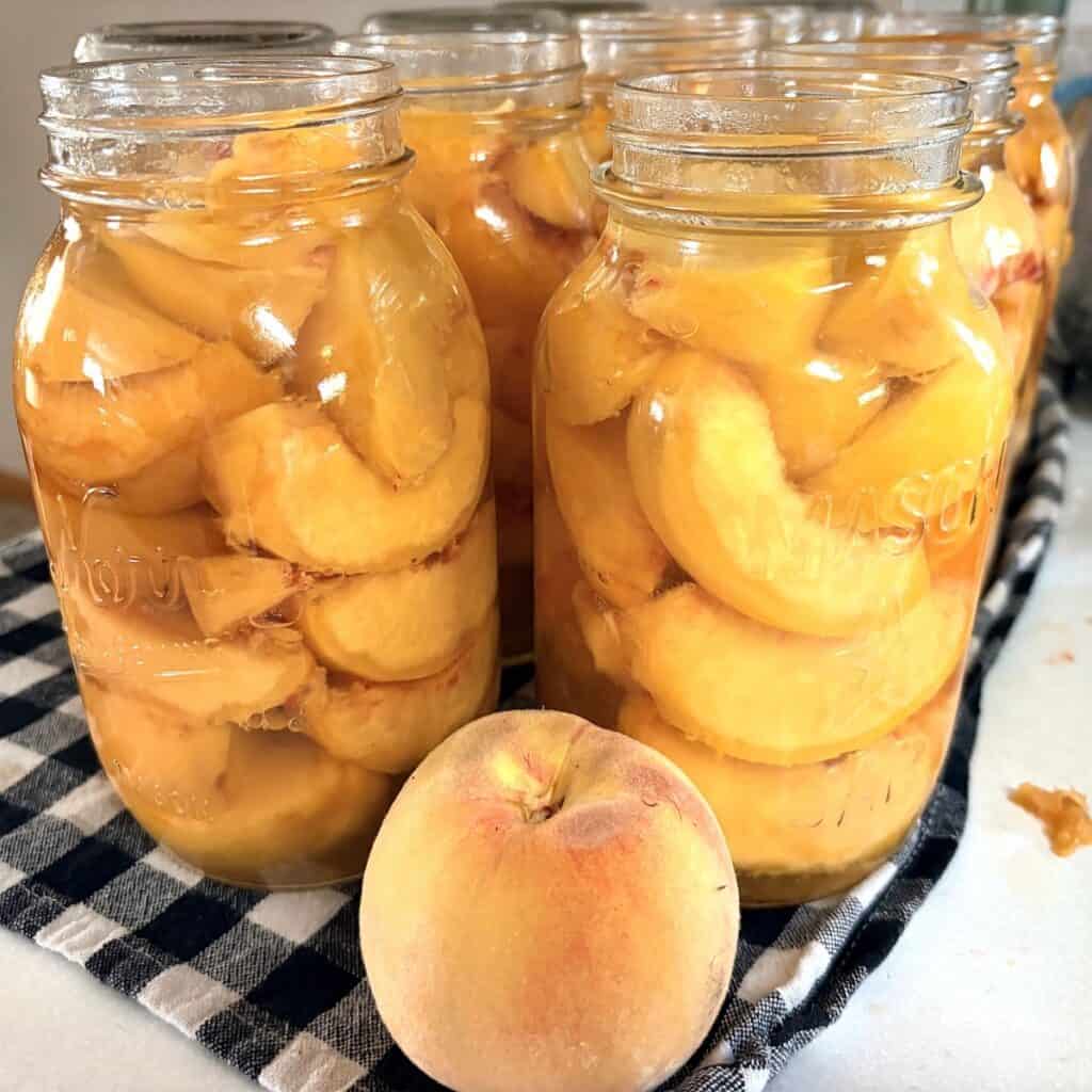 peaches in quart canning jars ready to be canned and a fresh peach sitting next to them