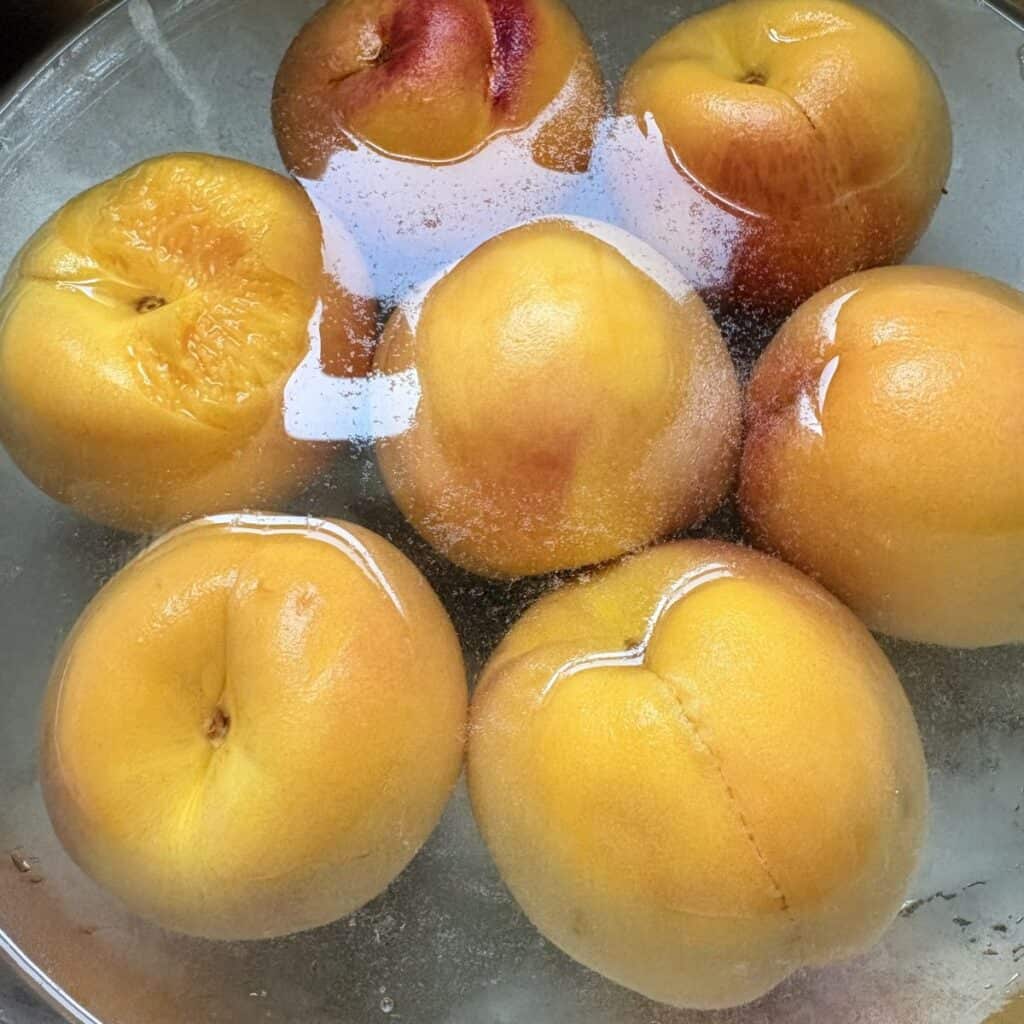 peaches in a cold water bath after being boiled to remove the skins
