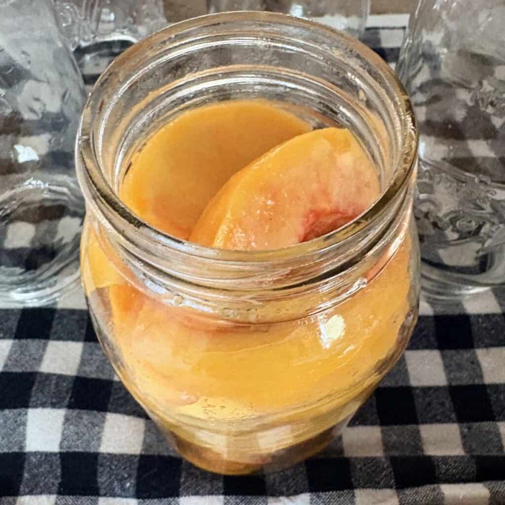fresh peaches in a canning jar sitting on a black and white towel