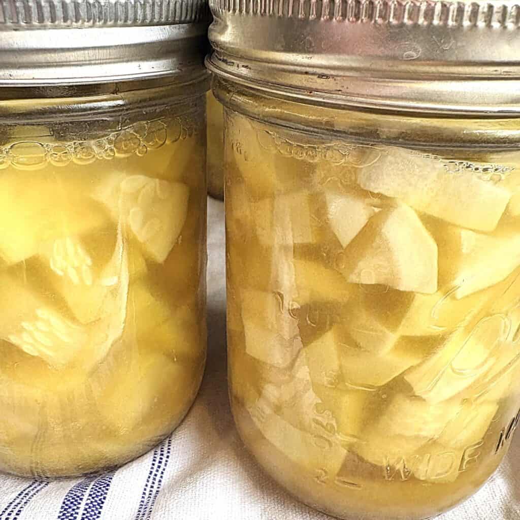 jars of canned zucchini pineapple sitting on a white kitchen towel